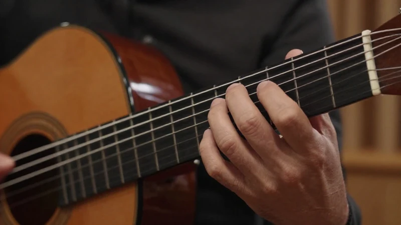 Primer plano de las manos de un guitarrista posicionadas sobre el mástil de una guitarra clásica.