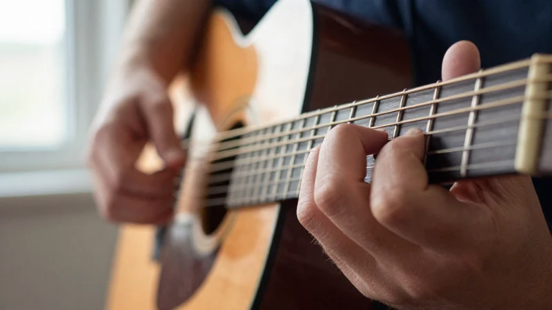 Primer plano de los dedos de un guitarrista pulsando una cuerda de acero en una guitarra acústica.