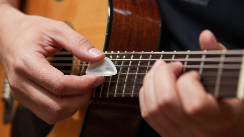 Primer plano de las manos de un guitarrista usando una púa y técnica de dedos sobre cuerdas de acero.