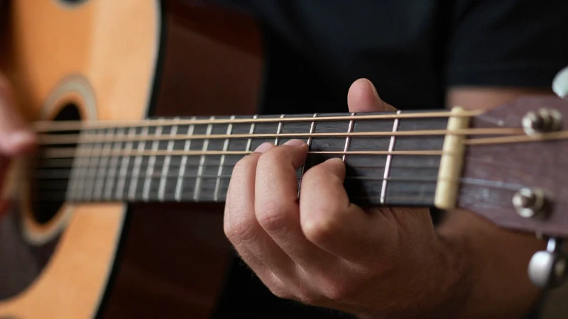 Primer plano de los dedos de un guitarrista ejecutando notas precisas sobre las cuerdas de una guitarra acústica.