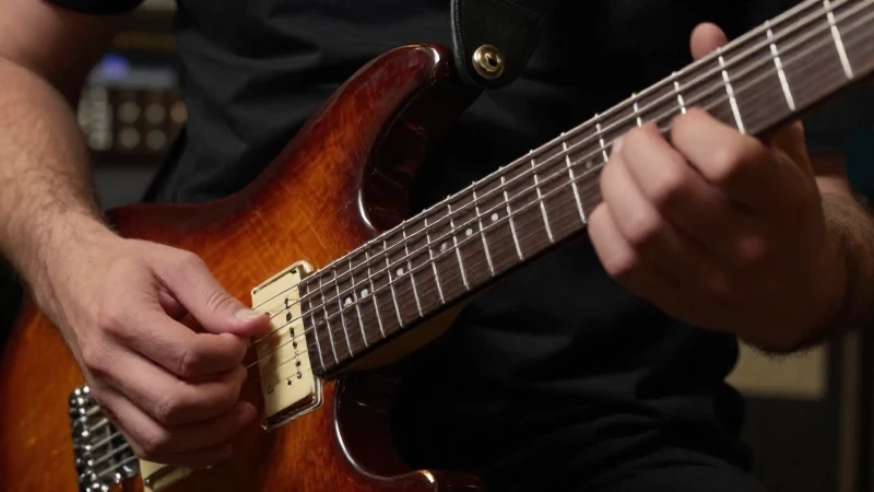 Primer plano de las manos de un guitarrista realizando una técnica de barrido sobre las cuerdas.