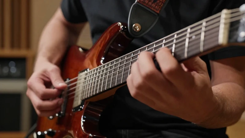 Manos de un guitarrista realizando una técnica de barrido sobre las cuerdas de una guitarra eléctrica.
