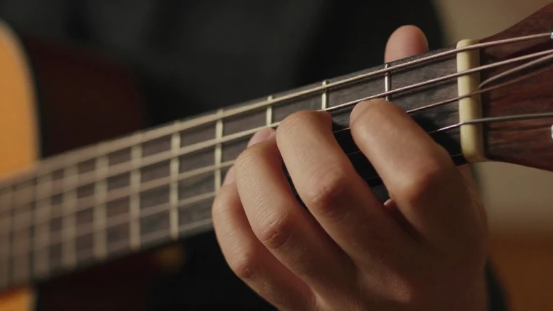 Primer plano de los dedos de un músico presionando cuerdas de nailon sobre un diapasón de madera.